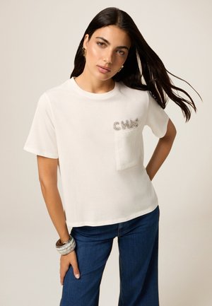 T-shirt blanc à manches courtes, avec une poche à l'avant et "CHIC" orné de strass argentés. Le tissu semble doux et décontracté. Associé à un jean bleu.