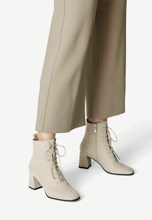 Beige mockakängor med fyrkantig tå, snörning framtill, dragkedja på sidan och 7 cm klack. Kombinerade med skräddarsydda beige byxor.