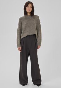 Grauer Strickpullover mit weitem Schnitt und Rundhalsausschnitt, kombiniert mit dunklen, weit geschnittenen Hosen mit gefaltetem Design und Knopfakzent.