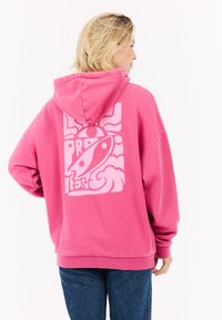 Haut à capuche rose avec une coupe décontractée et un grand graphique rose clair au dos, mettant en avant des vagues abstraites et un élément central de design.