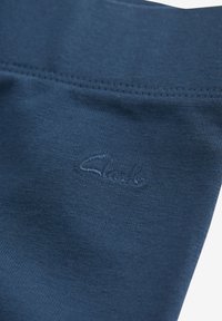 Tessuto blu navy con una texture morbida, caratterizzato da un logo in rilievo ricamato sulla parte anteriore. Dettagli delle cuciture lungo i bordi.