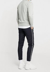 Maglione grigio a maglia, pantaloni tapered blu navy con strisce laterali bianche e sneaker bianche. Tessuto liscio, design informale, silhouette aderente.