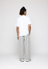 Camiseta de algodón blanca, de corte holgado, combinada con pantalones de pierna ancha de color gris claro y zapatillas blancas. Gorro de punto negro, cabello rizado, accesorios mínimos.