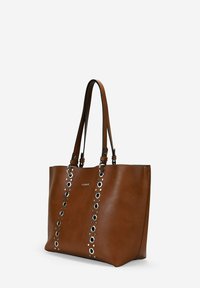 Sac fourre-tout en cuir marron avec des œillets en argent et des poignées doubles. Présente une forme rectangulaire et une texture lisse.