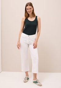 Grön ärmlös topp, vita cropped byxor och grå sneakers med gröna detaljer. Slät tyg och figurnära design. Enkel knappstängning.