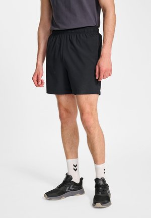 Zwarte sportshorts met een elastische tailleband, gemaakt van lichtgewicht stof. Draagt witte sneakers en witte sokken met een chevronpatroon.