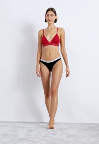 Raudonas trikampis liemenėlė su nėriniu apvadu; juodi kelnaitės su baltu liemeniu. Glotnus audinys, minimalistinis dizainas, prigludusi stilius.