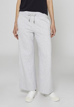 Pantaloni sportivi grigi chiaro a gamba larga realizzati in tessuto morbido, con vita regolabile con coulisse e texture liscia. Abbinati a scarpe da ginnastica bianche.