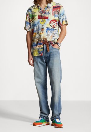 Korte mouwen, meerkleurige shirt met grafische prints, gecombineerd met vervaagde blauwe jeans en levendige, meerkleurige sneakers.