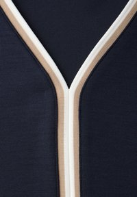 Marineblauer Stoff mit V-Ausschnitt, der von einem beigen und weißen Rippenbesatz gesäumt ist und ein gestreiftes Lagenmuster bildet.