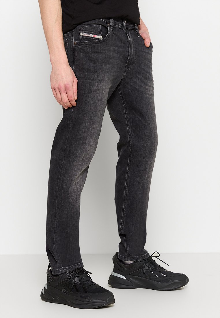 Dunkelblaue Jeans mit geradem Schnitt, featuring eine verblasste Textur, klassisches Fünf-Taschen-Design und dezente Markenkennzeichnung am Bund. Stylisch kombiniert mit schwarzen Sneakern.