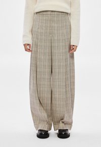 Calças de perna larga bege com um padrão às quadrículas em castanho e azul. Criam uma forma volumosa com pregas frontais e um cós alto.