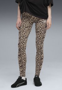 Beige legging met luipaardprint en zwarte vlekken, gemaakt van rekbaar materiaal, gecombineerd met zwarte sneakers met witte accenten.