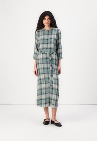 Grønn rutete midikjole med knappefront, trekvart ermer og matchende belte. Laget av lett stoff med en myk tekstur.