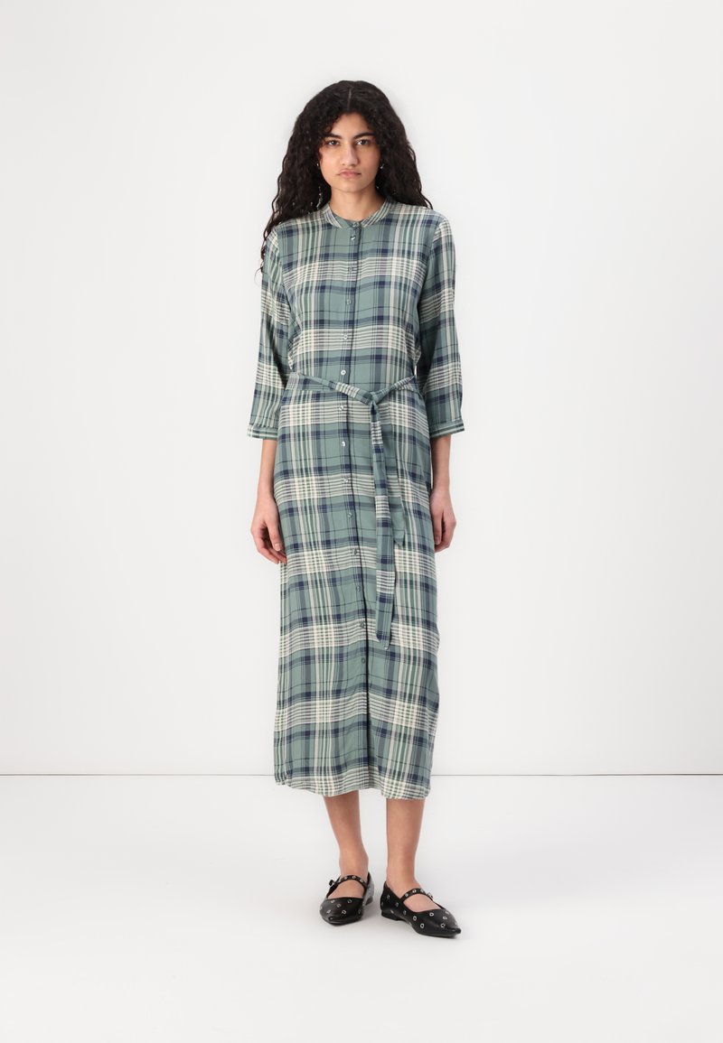 Grønn rutete midikjole med knappefront, trekvart ermer og matchende belte. Laget av lett stoff med en myk tekstur.