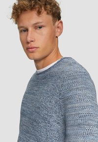 Lichtblauwe gebreide trui met een gestructureerd patroon, ronde halslijn en een comfortabele pasvorm, gepresenteerd op een model tegen een effen achtergrond.