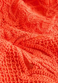 Tissu orange vif avec des motifs de broderie bouclée en relief complexes et des coutures texturées.