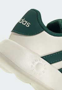 Zapatilla Adidas con parte superior sintética verde y suela de goma blanca, con acabado texturizado y detalle de logo bordado en el talón.