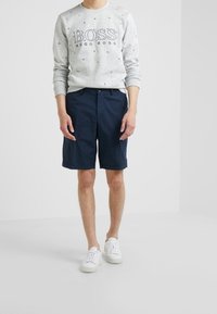Felpa grigia con motivi di ancore multicolori, logo "BOSS"; pantaloni corti blu navy; sneakers bianche. Abbigliamento casual con una vestibilità comoda.