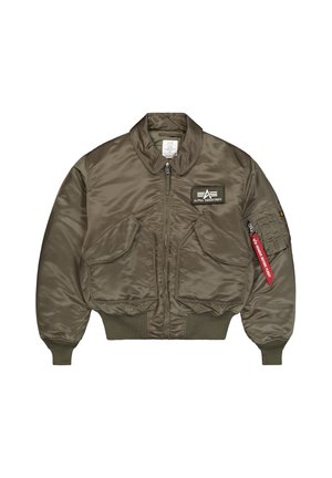 Olivgroene bomberjack met ritssluiting aan de voorkant, twee schuine klepzakken, geribbelde boorden, Alpha Industries-patch op de borst en een rode "Remove Before Flight" label op de mouw.