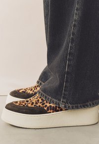 Baskets compensées imprimé léopard avec des accents en daim marron et une semelle blanche texturée, portées avec un jean en denim foncé.