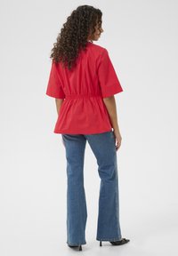 Top peplo rosso con maniche corte, vita elastica e scollatura rotonda. Abbinato a jeans a campana blu e scarpe con tacco nere.