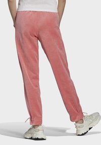 Rosa velourträningsbyxor med en avsmalnande design, elastisk midja och justerbara muddar. Matchas med klumpiga vita sneakers.