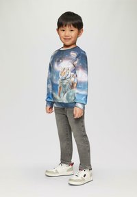 Blauwe sweatshirt met een tijger in een astronautenpak, versierd met een galaxiepatroon. Grijze jeans en witte sneakers met rode accenten maken de outfit compleet.