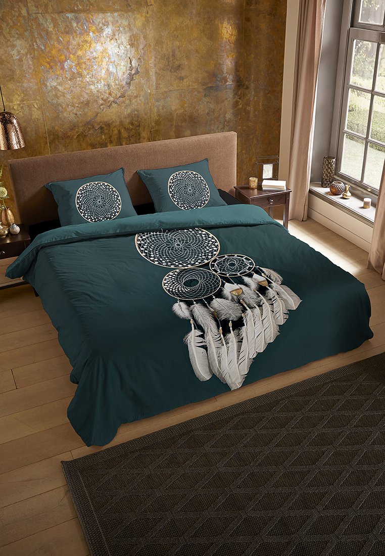 Teal beddengoed set met dromenvangerontwerp in het wit, met circulaire patronen en veren. Vergezeld van bijpassende kussenslopen op een houten bed.
