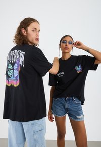 Black t-shirts with colorful butterfly graphics on the back and front, paired with denim shorts. Fabric is soft, with a relaxed fit.