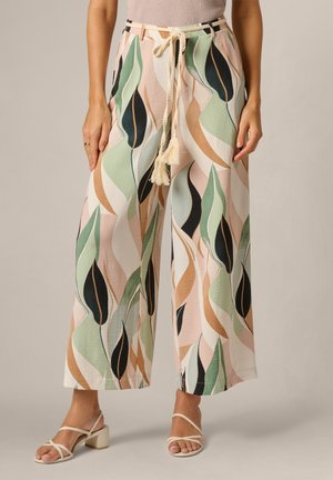 Frau trägt weite Hosen mit pastellfarbenem Blättermuster, Kordelzug in der Taille und beige Sandalen mit Absatz und Riemchen.