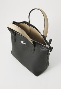 Black textured leather handbag with a beige handle and zipper. Features a small white logo on the front and open top for easy access.