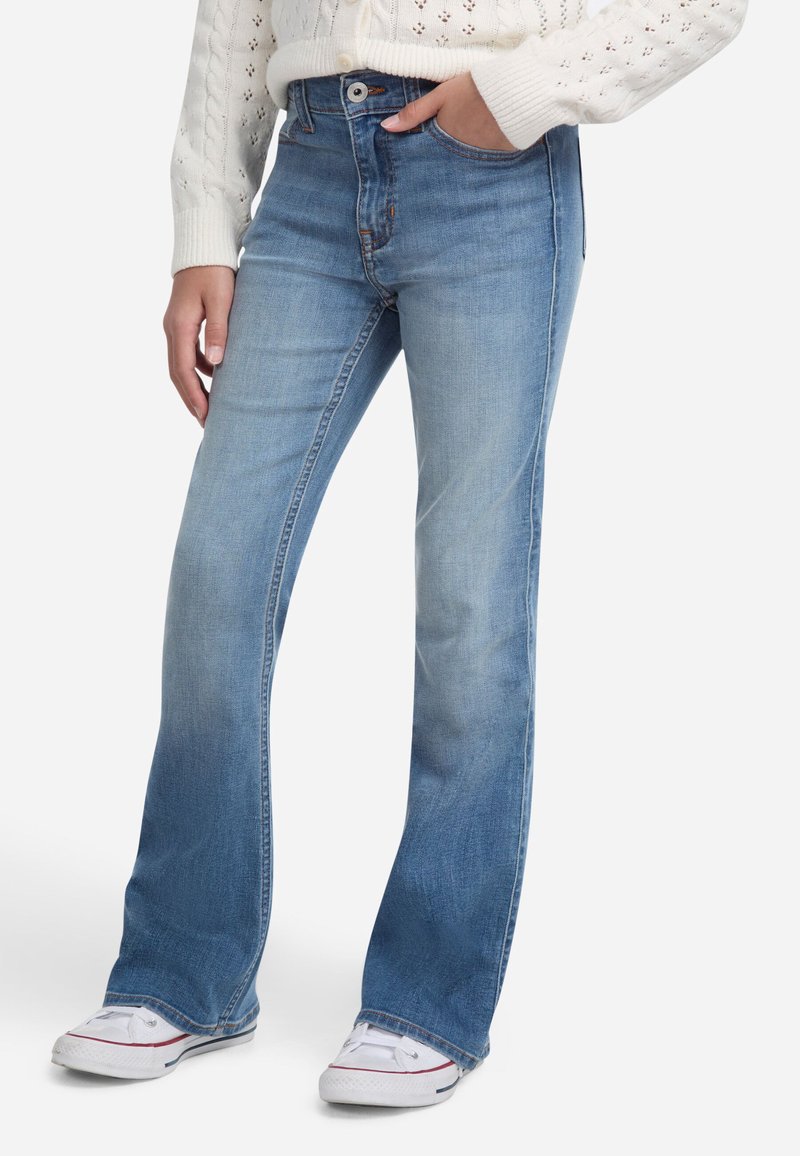 Jeans flare in denim azzurro chiaro con una leggera sfumatura, design a cinque tasche e cuciture visibili. Abbinati a sneakers bianche.