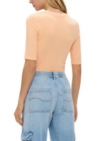 Pfirsichfarbiges, tailliertes T-Shirt mit kurzen Ärmeln, kombiniert mit hellblauen Jeans-Cargohosen mit zwei Gesäßtaschen und geschwungenen Nähten.