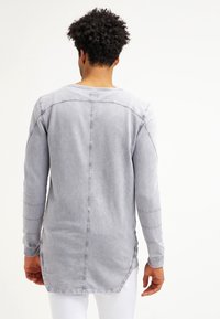 Camicia in denim grigia a maniche lunghe con orlo arrotondato, cuciture in contrasto e etichetta al collo. Il tessuto ha un aspetto morbido e usurato.