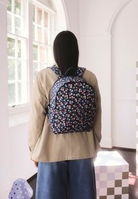 Sötétkék virágmintás hátizsák, többszínű virágmintákkal, párnázott pántokkal és kerekded formával. Az anyag tartósnak tűnik, sima textúrájú.