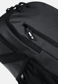 Zaino nero con esterno in nylon texturizzato, scomparti con zip, dettagli in rete e cursori con marchio. Design compatto e funzionale.