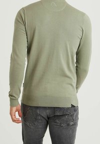 Pull en maille vert olive avec un col rond, des poignets et un ourlet côtelés, vu de dos, associé à un jean en denim gris foncé.