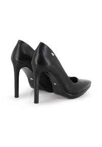 Par de zapatos de cuero negro de tacón alto con puntera puntiaguda y tacones stilettos delgados sobre un fondo blanco.