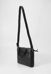 Svart skinnveske med rektangulær form, har to håndtak på toppen og en avtakbar stropp, inkluderer frontlommer med glidelås og en jevn tekstur.