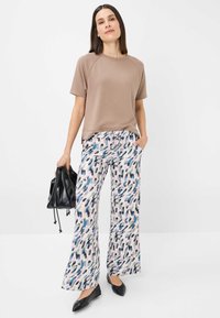 Beige t-shirt med korte ærmer, kombineret med mønstrede, løse bukser i lys pink, blå og grøn. Modellen holder en sort snørebåndstaske.