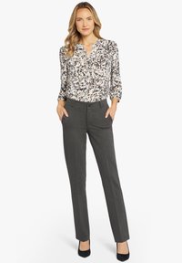 Bluse med blomsterprint i lyse nuancer med knaplukning ved halsen, parret med mørkegrå skræddersyede bukser og sorte hæle. Glat stofstruktur.