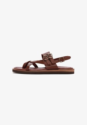 Sandal de cuero marrón con tiras cruzadas, hebilla ajustable, suela plana, textura suave y un diseño casual.