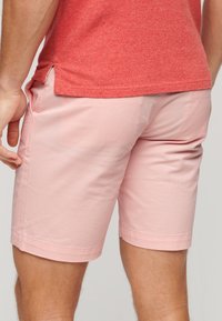 Pantalones cortos de color rosa claro, hechos de una tela suave, con un corte relajado, bolsillos laterales y un borde rematado. El fondo es de un gris neutro.