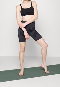 Černá sportovní podprsenka a odpovídající cyklistické šortky s vysokým pasem, vyrobené z elastické tkaniny, s hladkou texturou a minimalistickým designem.