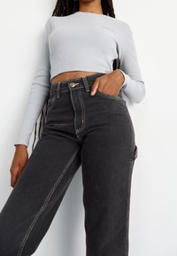 Top corto de manga larga de rayas grises con escote redondo combinado con jeans de mezclilla negros de tiro alto con costuras blancas en contraste.
