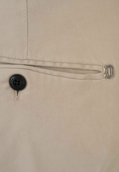 Tessuto beige con una superficie texturizzata presenta un bottone nero e un accento metallico. È visibile una tasca con una cucitura orizzontale.