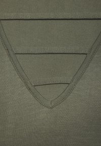 Camiseta verde oliva de cuello en V con una textura suave. Presenta tela de doble capa en el escote y costuras reforzadas a lo largo de los bordes.