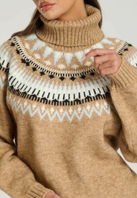 Beige polotröja med mönstrad yoke som har blå, creamfärgade och svarta geometriska mönster. Texturerat, mysigt stickat tyg.