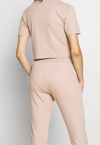 Kortärmad, pudrig rosa croppad topp i kombination med matchande tapered byxor. Mjuk bomullsmaterial med en jämn yta och sidofickor.